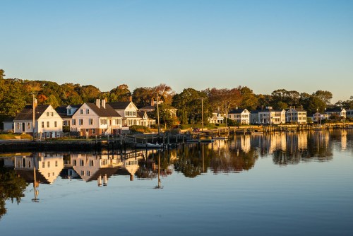 A serene waterfront scene with white houses reflecting in calm water during sunset.