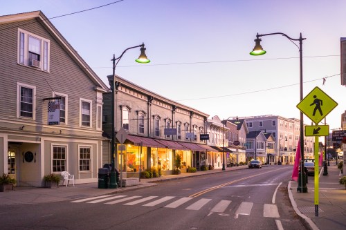 A quiet street at dusk, featuring charming shops, streetlights, and a pedestrian crossing sign.