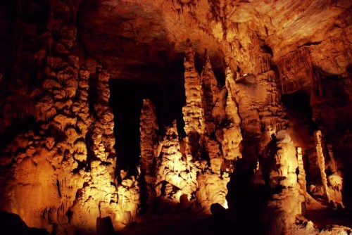 Stalactites and stalagmites illuminated in a dark cave, showcasing intricate rock formations.