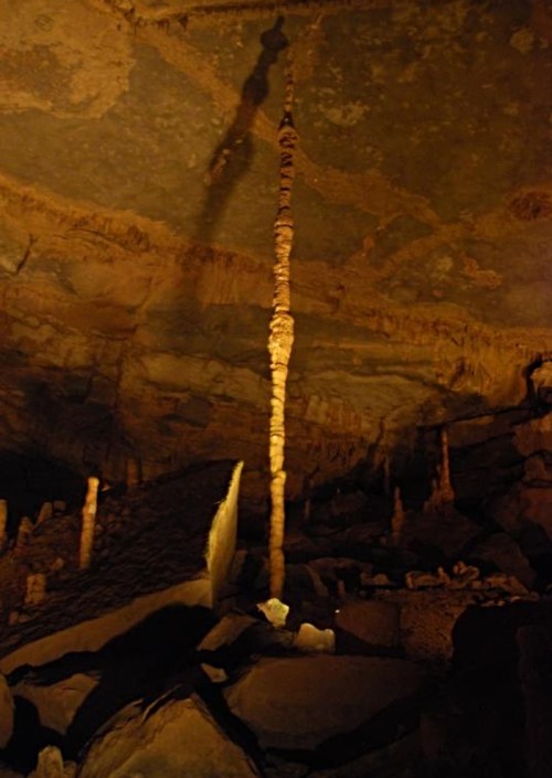A tall stalagmite rises from the cave floor, illuminated against the rocky cave walls and ceiling.