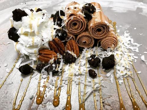 Delicious rolled ice cream topped with whipped cream, pecans, chocolate crumbles, coconut flakes, and caramel drizzle.