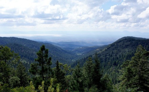 A panoramic view of lush green mountains and valleys under a cloudy sky, showcasing a serene natural landscape.