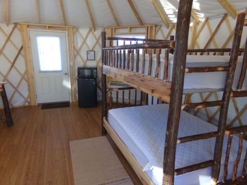 Interior of a cozy yurt featuring a bunk bed, a small fridge, and a door leading outside. Natural wood accents.