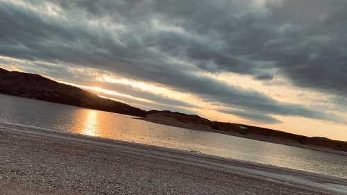 A serene lakeside view at sunset, with clouds reflecting on the water and mountains in the background.