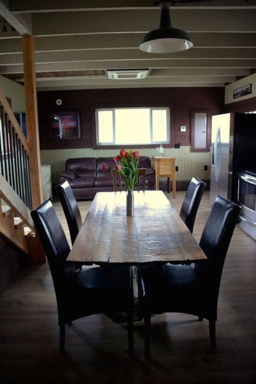 A cozy dining area with a wooden table, black chairs, and a vase of tulips, featuring a staircase and kitchen appliances.