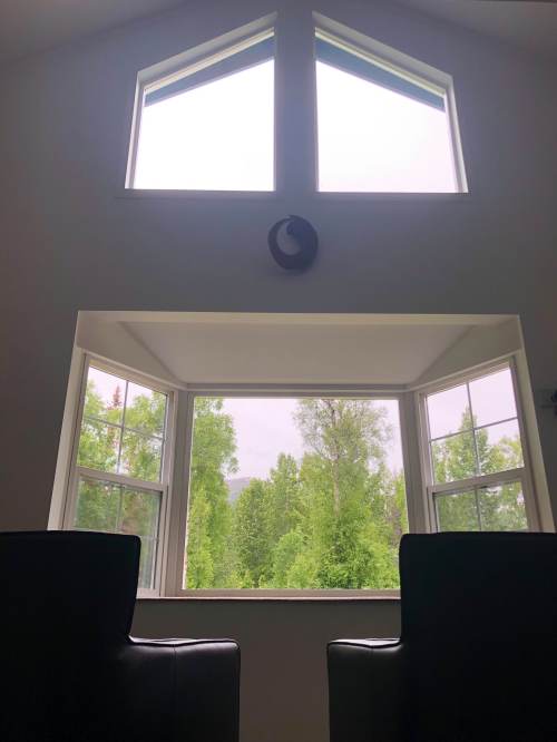 A cozy room with two chairs facing a large window, showcasing a view of green trees outside.