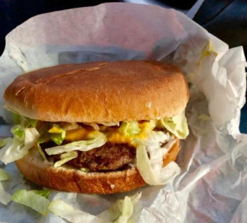 A hamburger with lettuce, cheese, and a beef patty, served in a paper wrapper.
