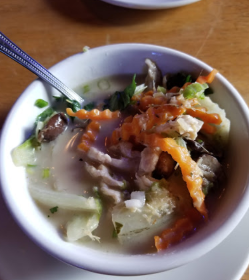 A bowl of soup with shredded chicken, vegetables, and garnished with carrots and herbs.