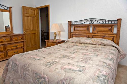 A cozy bedroom featuring a wooden bed frame, patterned bedding, a bedside lamp, and a dresser against a light wall.