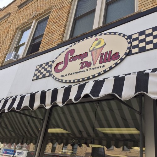 Sign for "Scoop De Ville" featuring an ice cream cone, with a checkered border and striped awning.