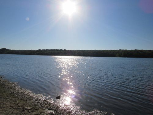 A bright sun shines over a calm lake, creating sparkling reflections on the water's surface.