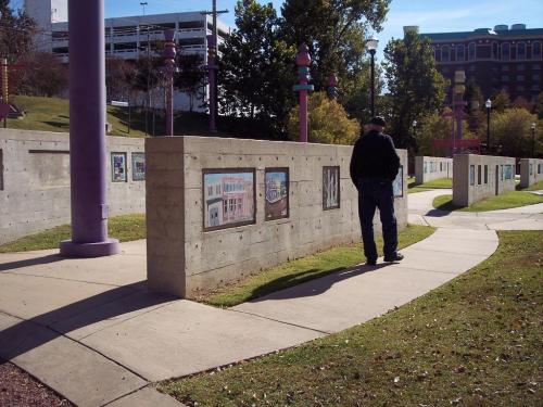 A person walks along a curved path beside concrete walls displaying colorful artwork in a park setting.
