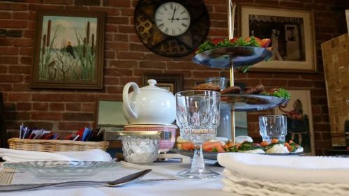 A beautifully set table with a tiered stand of snacks, a teapot, and decorative items against a brick wall backdrop.