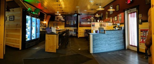 Interior of a rustic restaurant with wooden decor, bar area, and seating, featuring a cooler and various wall decorations.
