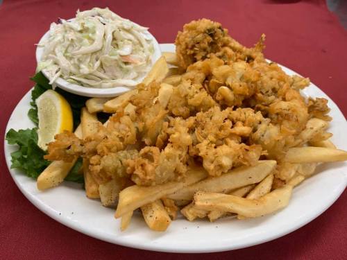 A plate of fried seafood, golden fries, coleslaw, and a lemon wedge on a red tablecloth.