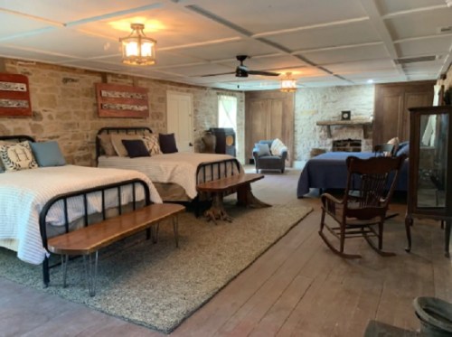 Cozy room with two beds, a fireplace, seating area, and rustic decor, featuring wooden floors and warm lighting.