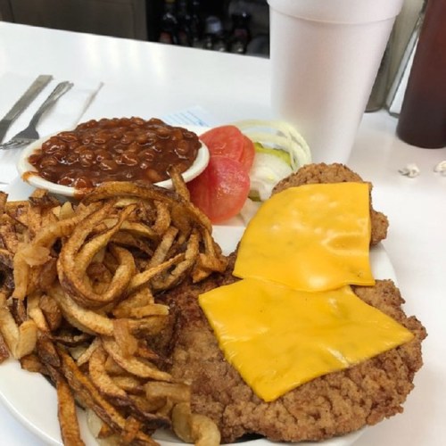 A plate of fried chicken topped with cheese, served with curly fries, baked beans, and fresh vegetables.