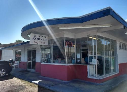 A small, colorful storefront with a sign reading "Kevin's Korner" and an "Open" neon sign in the window.