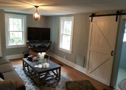 Cozy living room with a TV, wooden coffee table, and a sliding barn door, featuring natural light from windows.