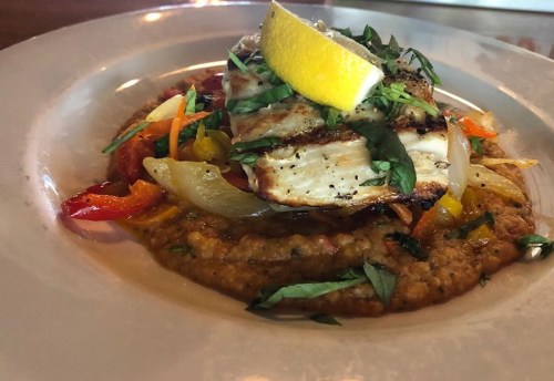 Grilled fish fillet topped with lemon, served on a bed of creamy sauce and colorful sautéed vegetables.