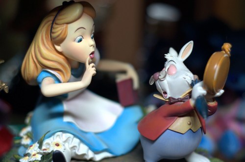 Alice and the White Rabbit share a secret moment, with Alice shushing and the Rabbit holding a pocket watch.