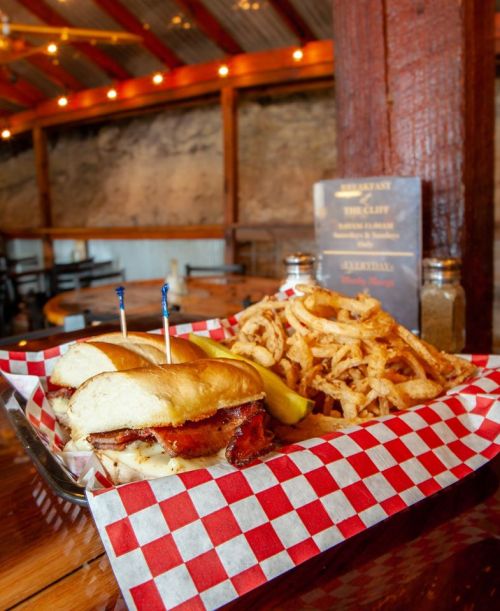 A delicious sandwich with bacon and two toothpicks, served with a side of crispy onion rings on a checkered plate.