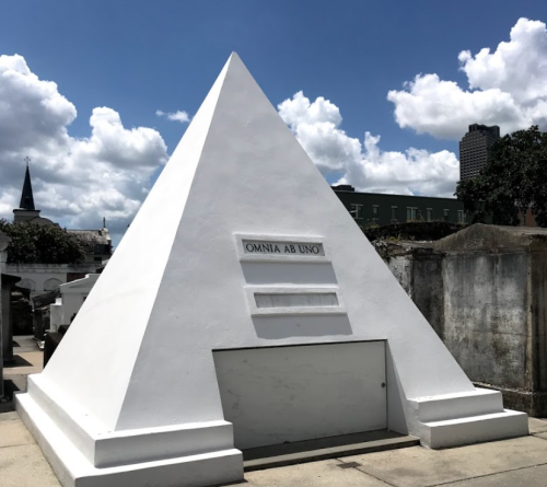 A white pyramid-shaped mausoleum with the inscription "OMNIA AB UNO" against a blue sky with clouds.