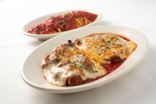 A plate of baked chicken parmesan topped with melted cheese, served with a side of spaghetti in marinara sauce.