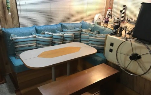 Cozy interior of a boat with a cushioned seating area, striped pillows, a table, and nautical decor.
