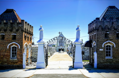 Entrance to Saint Roch Cemetery, featuring ornate gates and statues, under a clear blue sky.