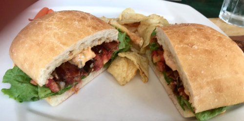 A close-up of a sandwich with lettuce, tomatoes, and sauce, served with potato chips on a white plate.