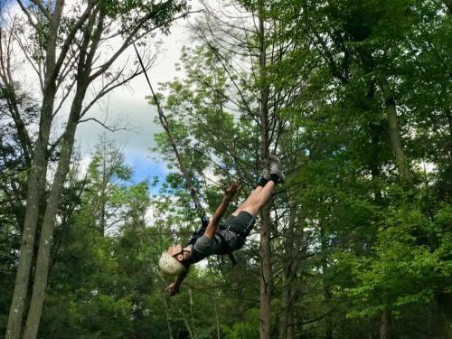 A person in a helmet swings through trees, suspended by a harness, enjoying an outdoor adventure in nature.