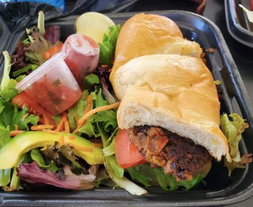 A sandwich filled with meat on a bed of mixed greens, accompanied by a side of salsa and dressing.