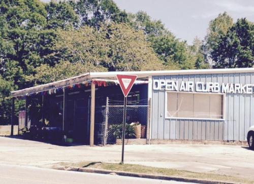 A blue building with "Open Air Club Market" signage, featuring a yield sign in front and trees in the background.