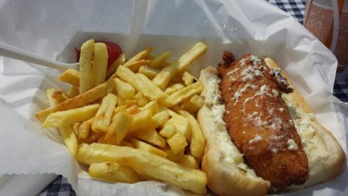 A plate with a fried fish sandwich topped with sauce, accompanied by a side of golden French fries.