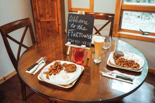 A cozy dining table with two plates of food, drinks, and a chalkboard sign welcoming guests to the Firetower.