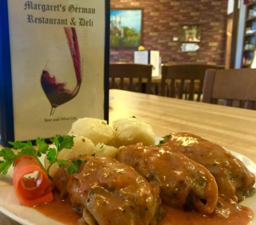 A plate of stuffed cabbage rolls in sauce, served with mashed potatoes and garnished with a carrot and parsley.