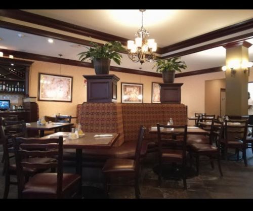 Cozy restaurant interior with wooden chairs, patterned booths, and potted plants, creating a warm dining atmosphere.