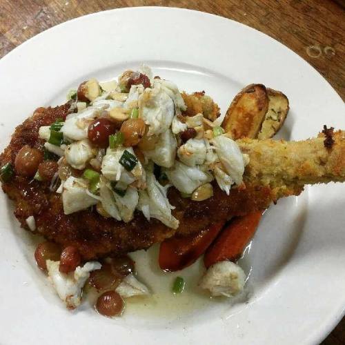A plate of fried fish topped with crab meat, onions, and herbs, served with roasted vegetables.