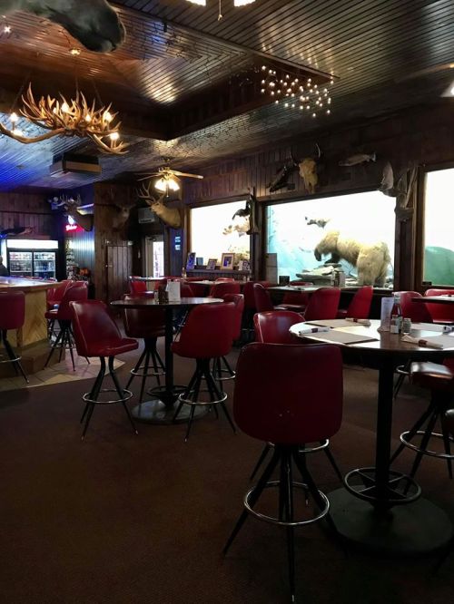 Cozy restaurant interior with red chairs, wooden decor, and mounted animal heads on the walls.