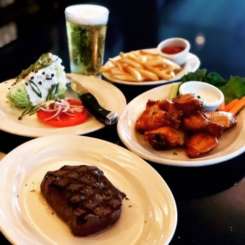 A delicious meal featuring steak, chicken wings, salad, fries, and a beer on a table.
