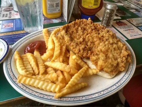 A plate of crispy fried chicken on a bun, served with crinkle-cut fries and a side of ketchup.