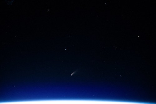 A comet streaks across a starry sky above the Earth's horizon, with a dark backdrop of space.
