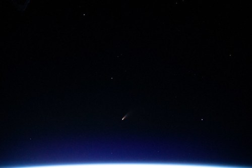 A comet streaks across the night sky above a curved horizon, dotted with stars.