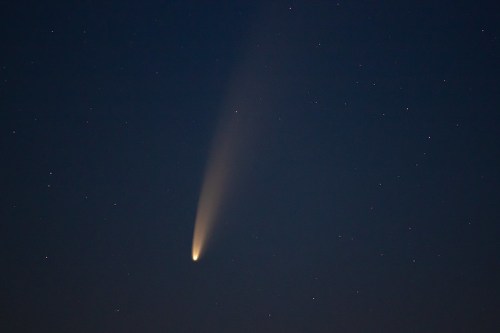 A bright comet with a long tail streaks across a dark night sky filled with stars.