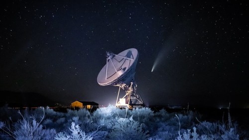 A satellite dish under a starry night sky, with a comet visible in the background.