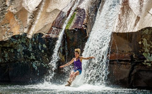 A child joyfully splashes in water while sliding down a rocky waterfall on a sunny day.