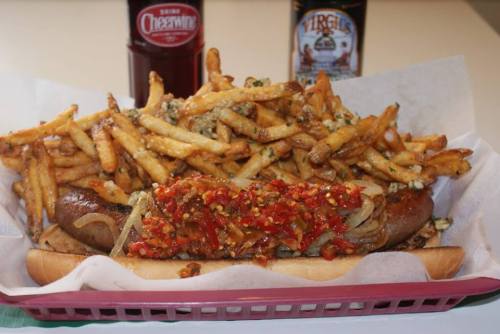 A loaded hot dog topped with onions and peppers, served with a generous side of crispy fries.