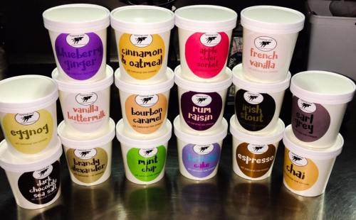 A display of various ice cream tubs with colorful labels, featuring flavors like blueberry ginger, chai, and bourbon caramel.
