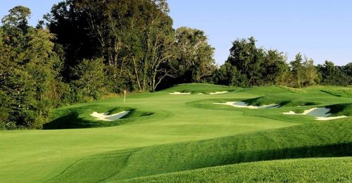 Lush green golf course with rolling hills and sand traps under a clear blue sky.
